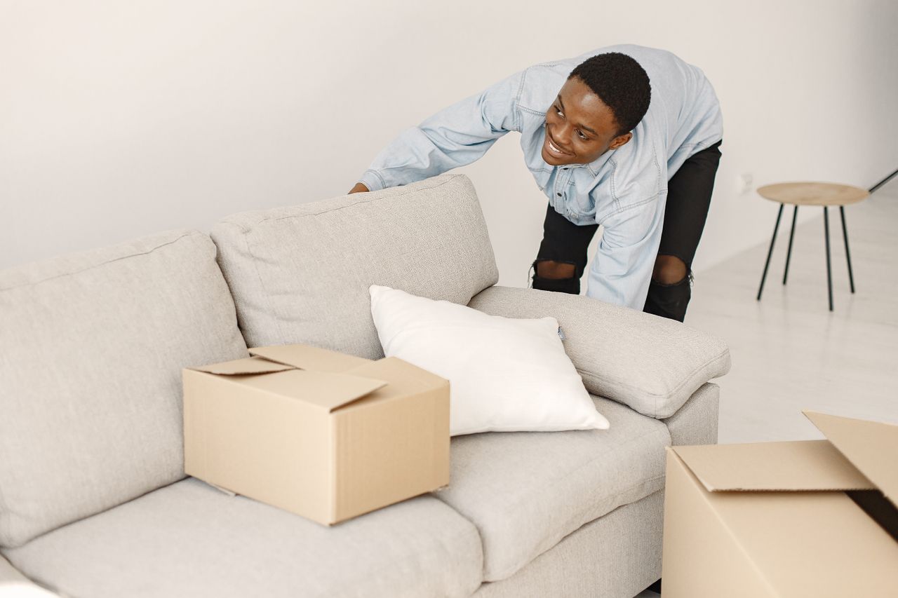 about-02 Young man smiling while organizing cardboard boxes in a contemporary living room.